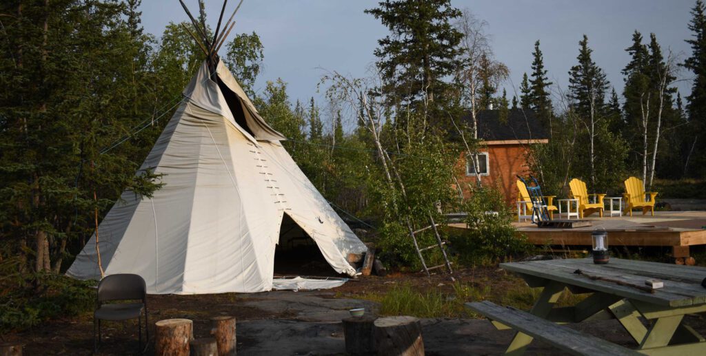 Teepee, cabin and dock with picnic table in foreground of forest in NWT